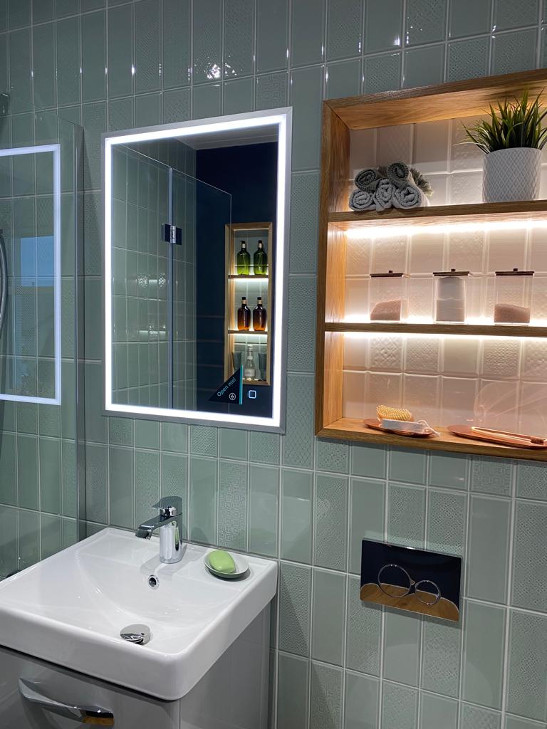 A green tiled bathroom with an open faced wooden shelving unit on the wall